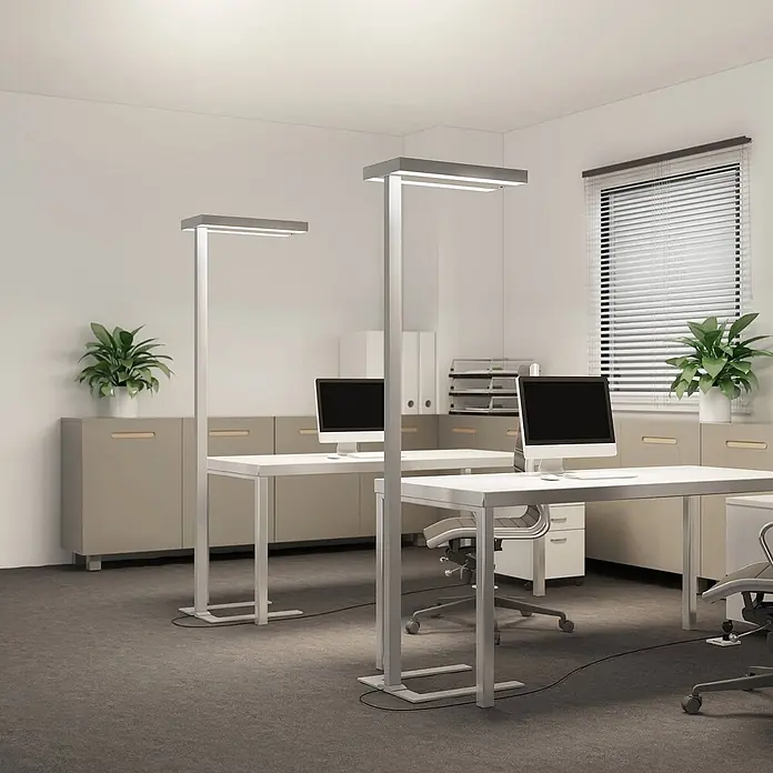 Arcchio Stehleuchte Logan Ultra - alu / grau / zink, alu / grau / zink - Zwei silberfarbene, moderne Stehleuchten mit rechteckigen Köpfen beleuchten einen Büroarbeitsplatz mit weißen Schreibtischen und Monitoren.