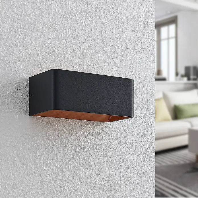 Arcchio Wandleuchte Karam - L x B x H: 10 x 20 x 8 cm, schwarz, schwarz - Dunkelgraue rechteckige Wandleuchte mit kupferfarbener Innenseite, an einer strukturierten weißen Wand in einem gemütlichen Raum.