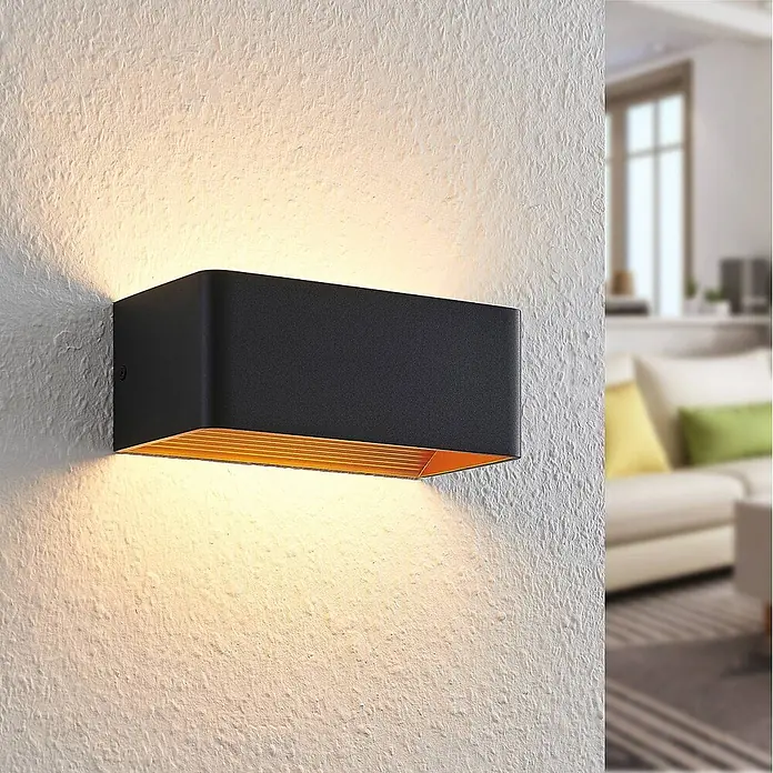 Arcchio Wandleuchte Karam - L x B x H: 10 x 20 x 8 cm, schwarz, schwarz - Moderne schwarze Wandleuchte mit goldener Innenseite, die warmes Ober- und Unterlicht auf eine strukturierte Wand wirft.