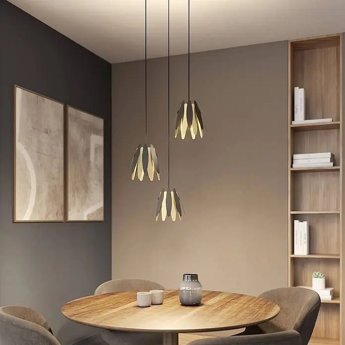 Lucande Pendelleuchte Lounit - L x B x H: 50 x 50 x 150 cm, schwarz, Schwarz, gold, E14 - Drei Pendelleuchten mit dunklen und hellen blütenblattähnlichen Elementen über einem Holzesstisch.