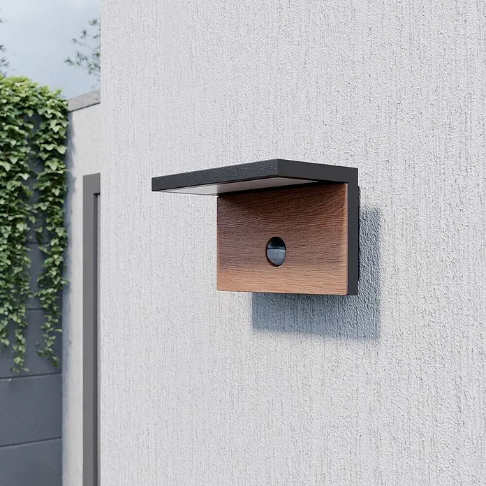 Lucande Außenwandleuchte Lignus - schwarz, IP54 - Außenwandleuchte mit schwarzem Metallrahmen, Holzfront und Bewegungssensor, an einer strukturierten Außenwand montiert.