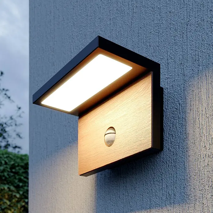 Lucande Außenwandleuchte Lignus - schwarz, IP54 - Moderne Außenwandleuchte mit schwarzem Rahmen, Holzoptik-Front und integriertem Bewegungsmelder, an einer Außenwand.