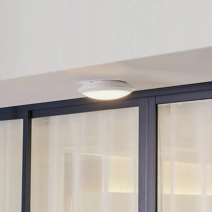 Lindby Außenwand- & Deckenleuchte Naira - weiß / opal, weiß / opal, IP65 - Weiße, beleuchtete LED-Deckenleuchte an einer Decke über Glastüren montiert.