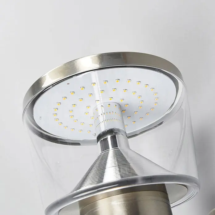 Lindby Außenwandleuchte Antje - alu / grau / zink, IP44 - Nahaufnahme einer LED-Leuchtkomponente mit runder weißer Platine, gelben Chips, transparenter Abdeckung und silbernen Metallakzenten.