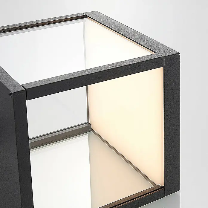 Lucande Außenwandleuchte Cube - schwarz, IP54 - Dunkelgraue, granulare Metall-Kubusleuchte mit Glaspaneelen, eine Seite beleuchtet.