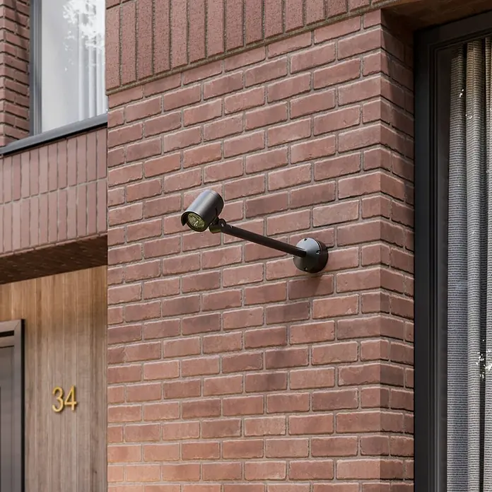 Lucande Außenwandleuchte Beatrix - schwarz, schwarz, IP65 - Schwarzer Metallstrahler mit langem Arm, an einer Ziegelfassade montiert zur Außenbeleuchtung.