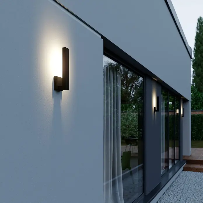 Lindby Außenwandleuchte Isadore - schwarz, schwarz, IP44 - Schwarze Außenwandleuchte beleuchtet eine moderne Gebäudefassade, mit Licht nach oben und unten.