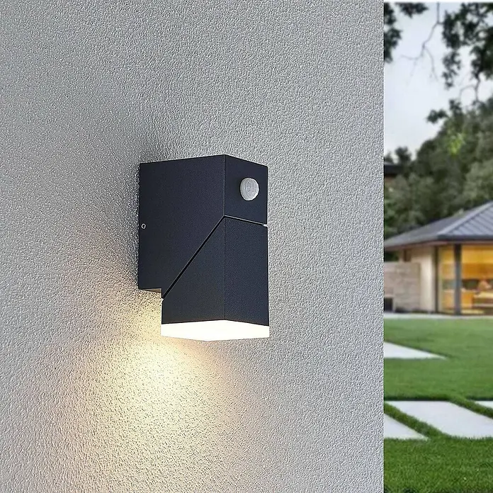 Lindby Außenwandleuchte Sally - schwarz, IP54 - Dunkelgraue, eckige Außenwandleuchte mit Bewegungsmelder, die warmweißes Licht auf eine strukturierte Wand wirft.