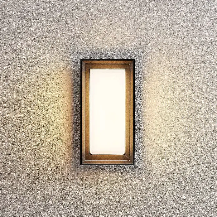 Arcchio Außenwandleuchte Ismera - schwarz, schwarz, IP65 - Rechteckige schwarze Wandleuchte mit goldfarbenem Innenrahmen, wirft warmes Licht auf eine strukturierte Wand.