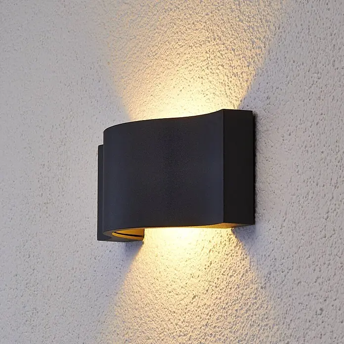 Lucande Außenwandleuchte Jace - schwarz, schwarz, IP54 - Dunkelgraue Außenwandleuchte an einer strukturierten Wand, die warmes Licht nach oben und unten wirft.