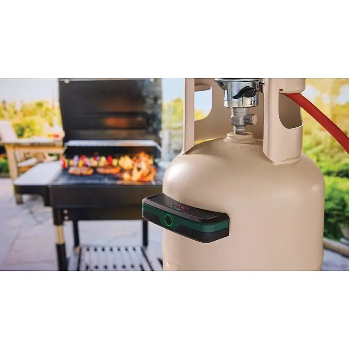 Bosch Gasflaschen-Füllstandsanzeiger Filio - Passend für: Stahl- und Aluminium-Flüssiggasflaschen (Propan und Butan) mit einem Durchmesser von 200-350 mm - Schwarz-grüner Bosch Filio Gasfüllstandsensor an einer beigefarbenen Propangasflasche, mit Grill im Hintergrund.