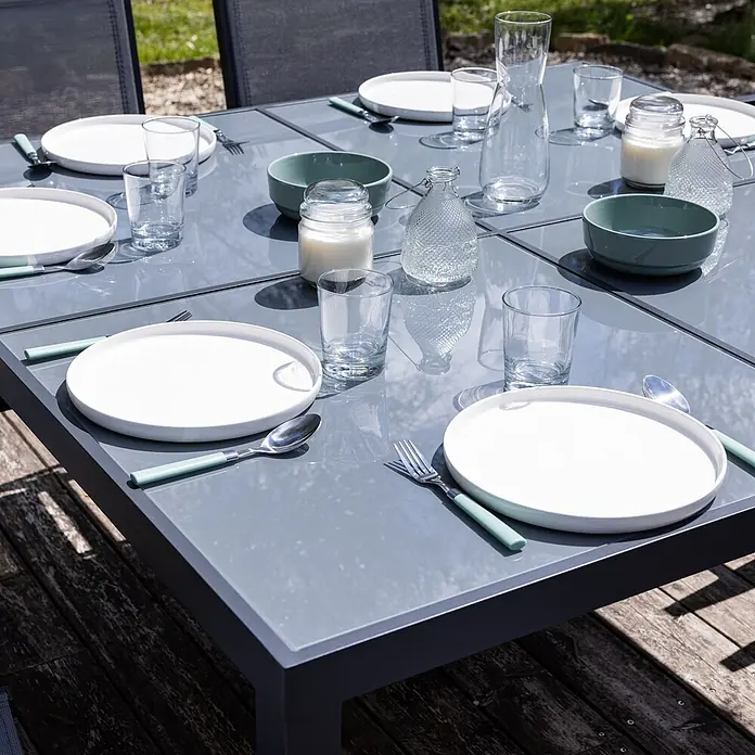Happy Garden Gartentisch-Set CAGLIARI - Gesamtumfang: 9 -tlg., Aluminium - Gedeckter Outdoor-Esstisch mit weißen Tellern, hellgrünen Schalen, klaren Gläsern und Besteck mit grünen Griffen.