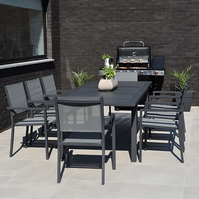Happy Garden Gartentisch-Set CAPRI - Gesamtumfang: 9 -tlg., Aluminium - Dunkelgraue Outdoor-Essgruppe mit Lamellentisch und sechs Stühlen aus Metall und Netzstoff auf einer Terrasse.