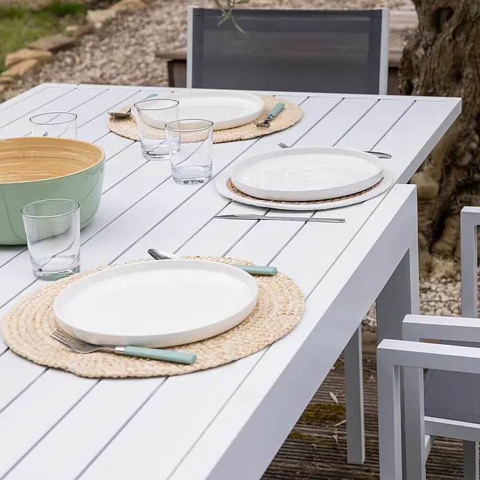 Happy Garden Gartentisch-Set VENEZIA - Gesamtumfang: 11 -tlg., Aluminium - Weißer Lamellen-Esstisch für draußen, gedeckt mit weißen Tellern, Gläsern und einer grünen Servierschale auf einer Terrasse.