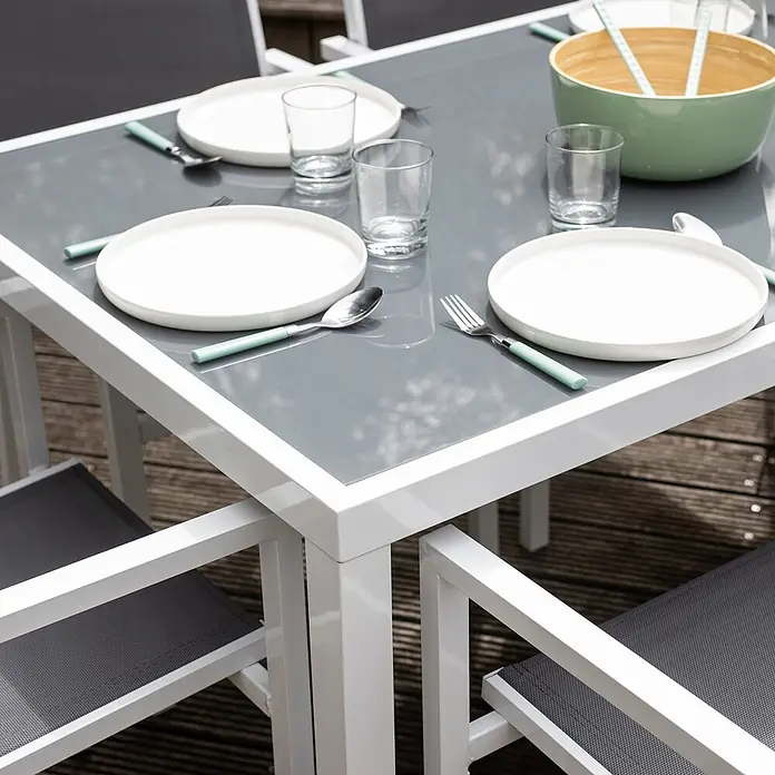 Happy Garden Gartentisch-Set BERGAMO - Gesamtumfang: 7 -tlg., Aluminium - Ein Outdoor-Essset mit weißem Tischgestell, grauer Tischplatte und grauen Netzstühlen, gedeckt mit weißen Tellern, Gläsern und mintgrünem Besteck.