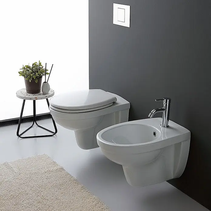 Kiamami Valentina Wand-WC-Kombination - Mit Spülrand, WC Abgang: Senkrecht, Weiß - Weiße wandhängende Keramiktoilette und Bidet mit Chromarmaturen in einem modernen Badezimmer.