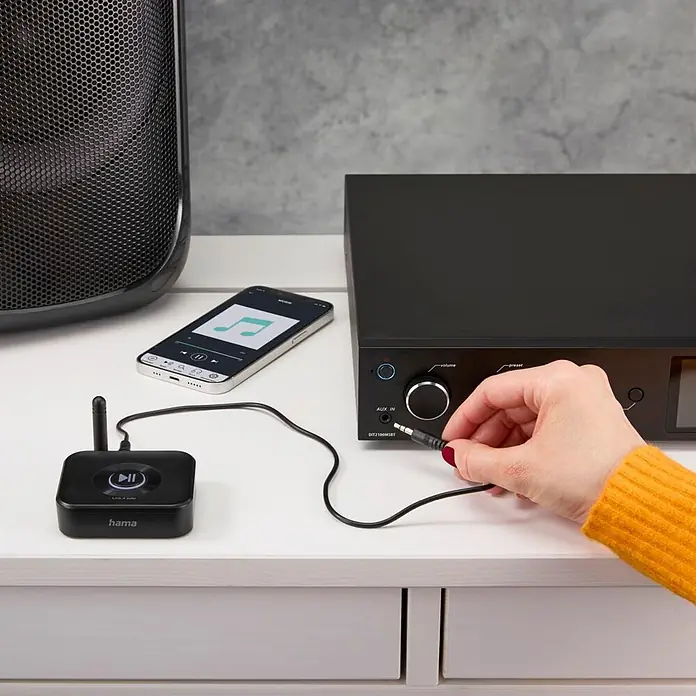 Hama Adapter 00205321 "Link.it solo" Empfänger Bluetooth nachrüsten an HiFi - Schwarz - Ein schwarzer Hama Bluetooth-Empfänger verbindet ein Smartphone (spielt Musik) über ein AUX-Kabel mit einem Audiosystem, von einer Hand gehalten.