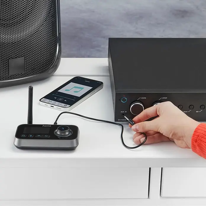 Hama Radio 00205322 "Link.it duo" Sender u. Empfänger Bluetooth nachrüsten - Schwarz - Hand steckt Audiokabel vom Hama Radio in AUX-Eingang des schwarzen Verstärkers, daneben Smartphone & Lautsprecher.