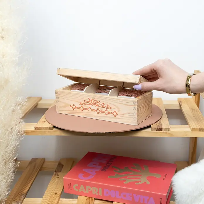 Creative Deco Speziallack Strukturpaste Feinkörnig 2 kg Ziegelrot - Rot, Sonstiges, 2 l, Sonstiges - Eine Hand öffnet eine helle Teekiste aus Holz mit orangefarbenem Muster, die Teebeutel mit Zitrustee auf einem Holzregal enthüllt.