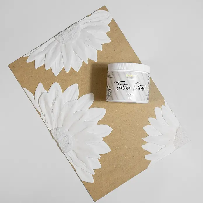 Creative Deco Speziallack Strukturpaste Glatt 1 kg Weiß - Weiß, Sonstiges, Sonstiges - Ein weißer Tiegel 'Creative Deco Texture Paste Smooth 1 KG' auf einer braunen Platte mit aufgetragenen weißen strukturierten Blumenformen.