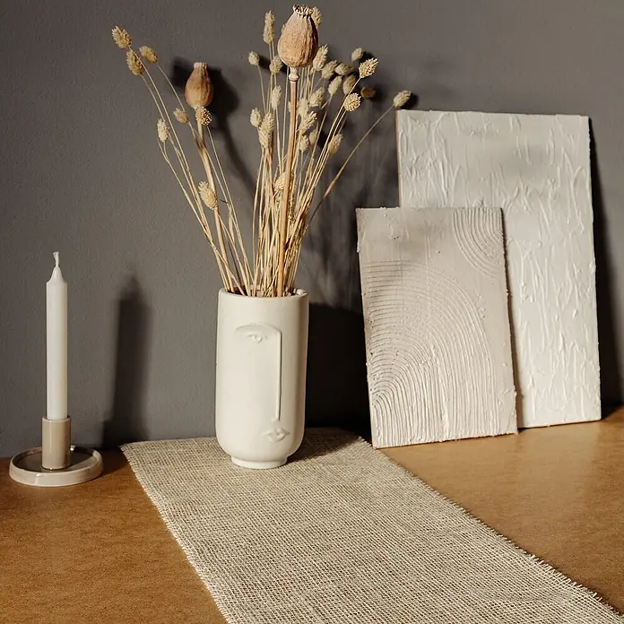 Creative Deco Bastelband Juteband Weiß 30cm x 10m - Weiß, 10 m - Eine Dekoration mit weißer Gesichtsvase, Trockenblumen, einer weißen Kerze und zwei texturierten weißen Kunstplatten auf einem Juteläufer.
