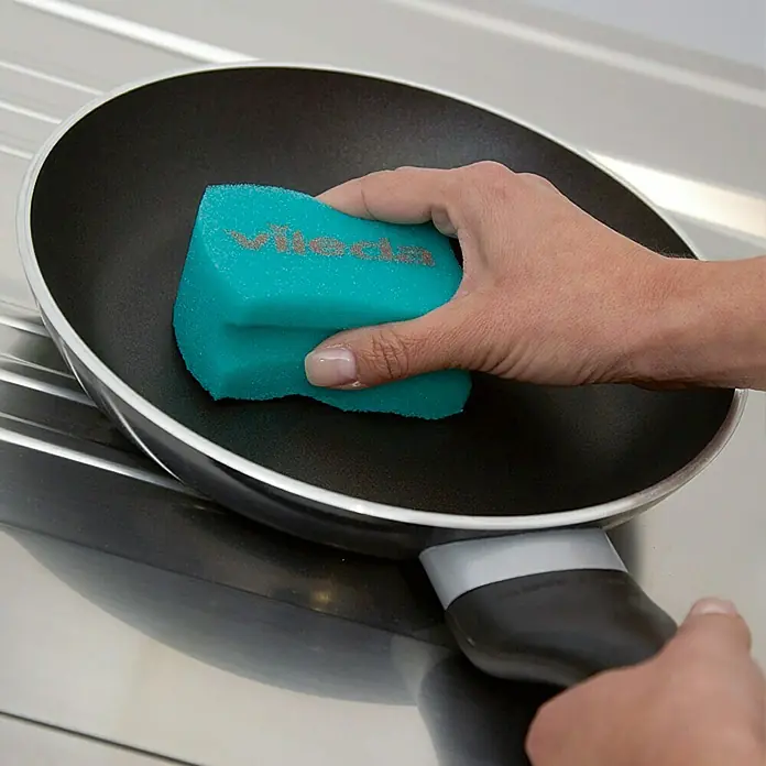 Vileda Glitzi Schwamm PUR Active - Glitzi Härtegrad: 1, 3 Stk. - Eine Hand reinigt eine schwarze Bratpfanne mit einem türkisfarbenen Vileda-Schwamm. Das Produkt ist ideal für die Reinigung von Töpfen und Pfannen.