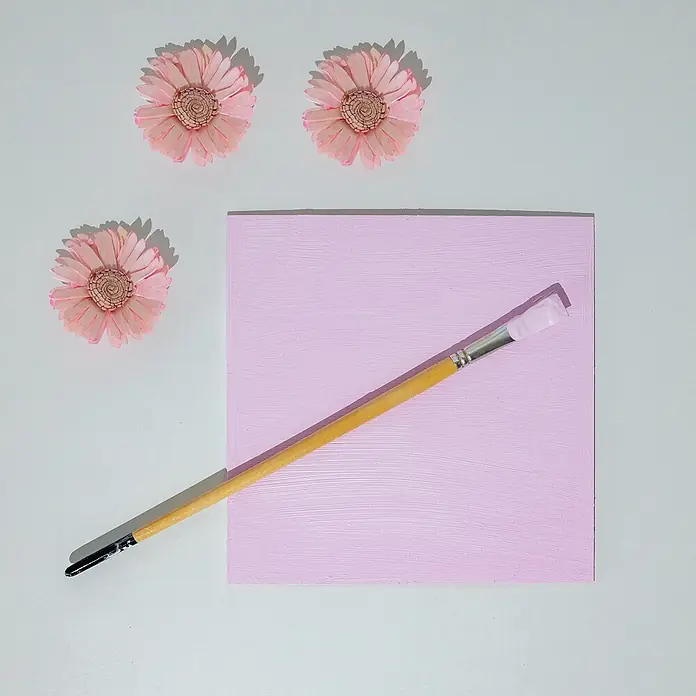 Creative Deco Speziallack Kreidefarbe für Möbel Rosa - Rosa, Matt, 1 l, Wasserbasiert - Hellviolette Leinwand mit Pinselstrichen, einem Pinsel und drei rosa Zierblumen.