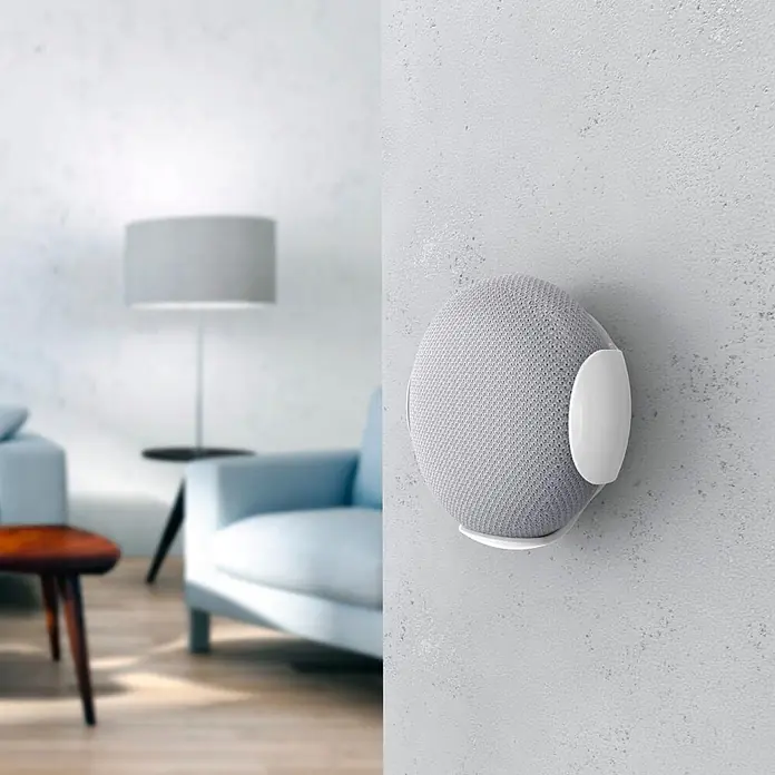 Hama Wandhalter 00220888 für Google Home/Nest mini - Weiß - Heller grauer kugelförmiger Smart Speaker mit weißer Halterung an grauer Wand in Wohnumgebung.