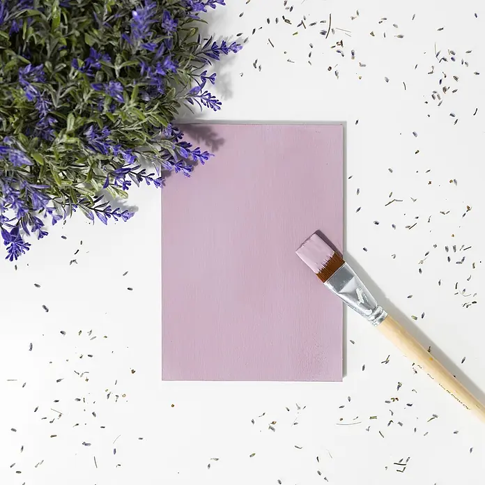 Creative Deco Fliederviolett Kreidefarbe für Möbel 1000 ml -  - Lavendelblüten und verstreute Blütenblätter um eine hellviolett bemalte Tafel mit einem Pinsel.