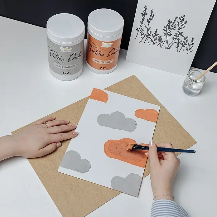Creative Deco Speziallack Strukturpaste Feinkörnig 2 kg Grau - Grau, Sonstiges, 2 l, Sonstiges - Zwei Dosen 'Fine-Grained Textur Paste' in Grau und Orange, von einer Person zum Malen von Wolken auf Leinwand verwendet.