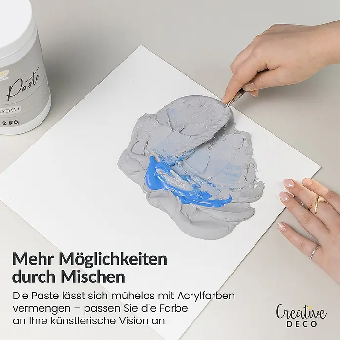 Creative Deco Speziallack Strukturpaste Feinkörnig 2 kg Grau - Grau, Sonstiges, 2 l, Sonstiges - Hand mischt graue Paste mit blauer Acrylfarbe auf weißer Oberfläche mit Spachtel; daneben Pastenbehälter.