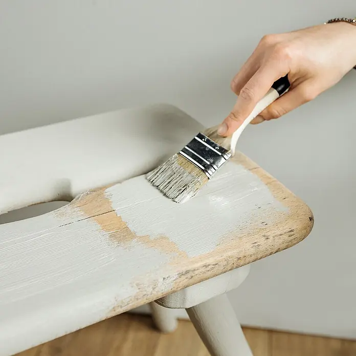 Creative Deco Speziallack Kreidefarbe für Möbel Kräutergrün - Grün, Matt, 1 l, Wasserbasiert - Eine Hand streicht einen Holzhocker hellgrau mit einem Pinsel an.