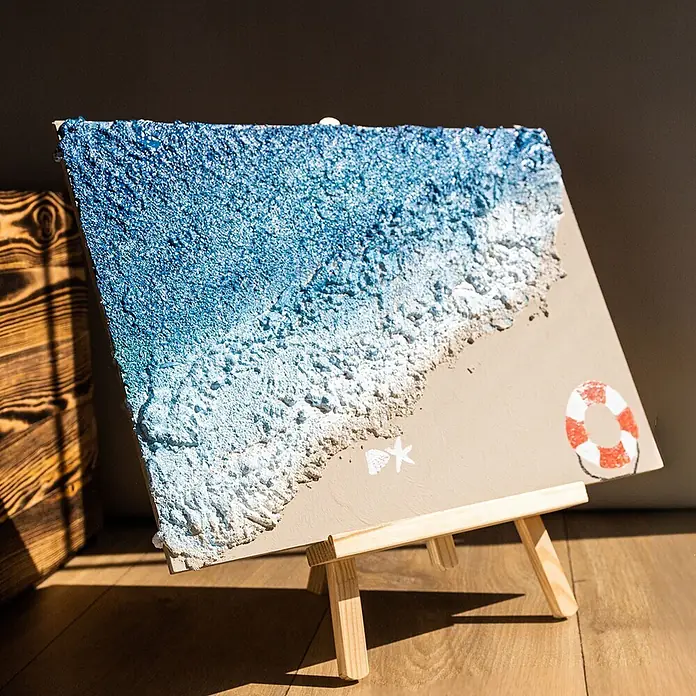Creative Deco Speziallack Strukturpaste Grobkörnig 1 kg Weiß - Weiß, Sonstiges, Sonstiges - Strukturiertes 3D-Strandkunstwerk auf Leinwand, das Wellen, Sand, Seestern, Muschel und Rettungsring zeigt, auf Holzstaffelei präsentiert.