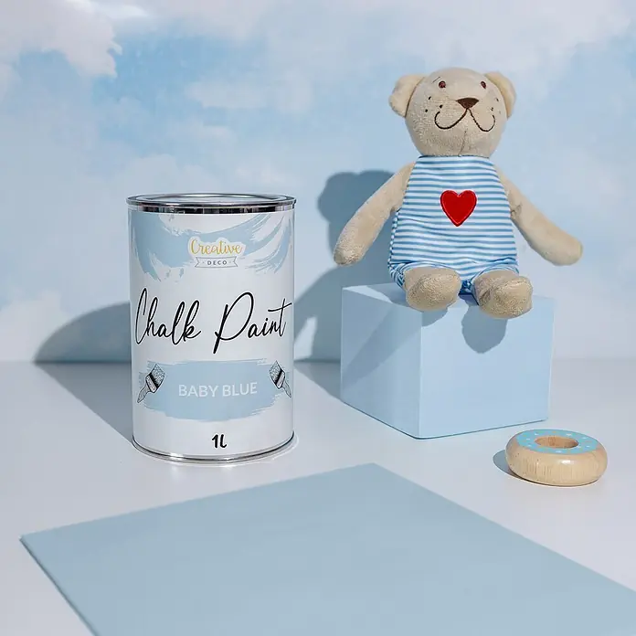 Creative Deco Speziallack Kreidefarbe für Möbel Hellblau - Blau, Matt, 1 l, Wasserbasiert - Babyblaue Kreidefarbe (1L) neben einem Teddybär und einem Holzspielzeug-Donut auf hellblauer Oberfläche.