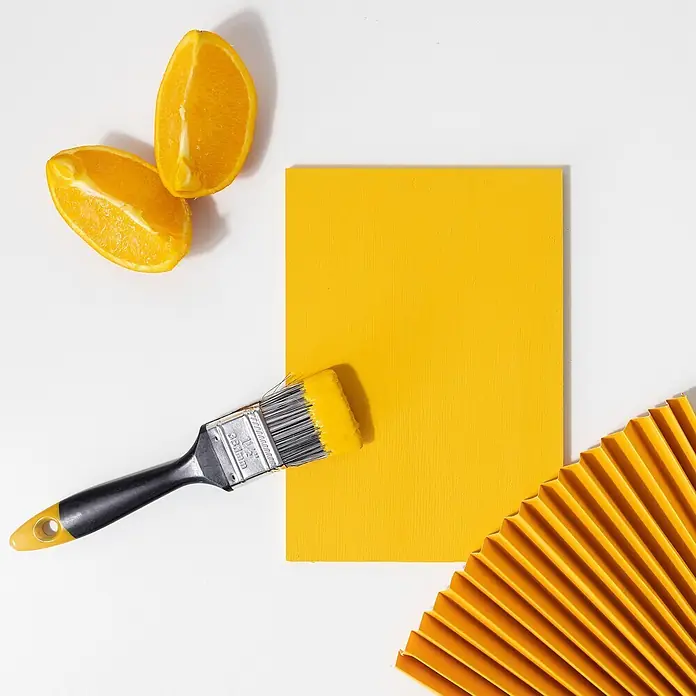 Creative Deco Speziallack Kreidefarbe für Möbel Orange - Orange, Matt, 1 l, Wasserbasiert - Pinsel mit gelber Farbe auf einem Holzbrett, begleitet von frischen Orangenscheiben und einem gelben Faltfächer.