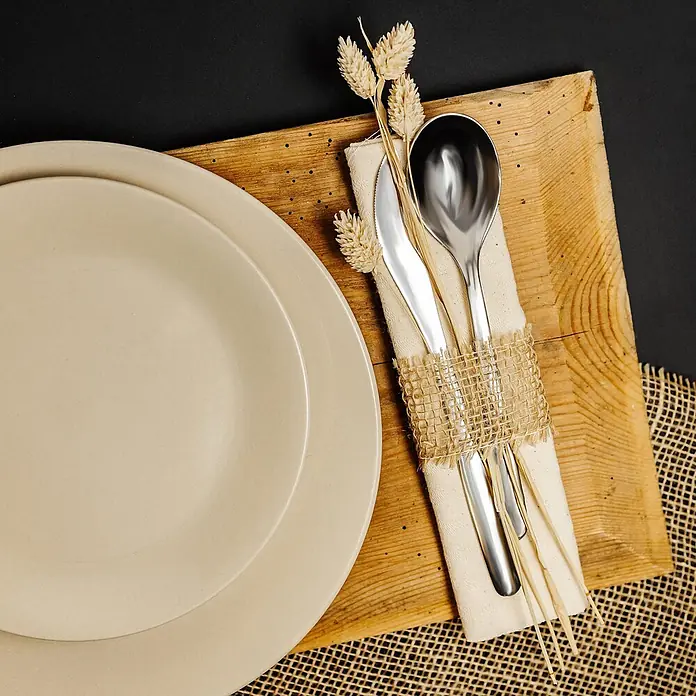 Creative Deco Bastelband Juteband 2 Rollen 5cm x 5m - Braun, 10 m - Ein rustikales Gedeck mit hellbeigen Tellern, Holzbrett und Besteck, in Leinen und Sackleinen mit getrocknetem Weizen, auf dunklem Grund.