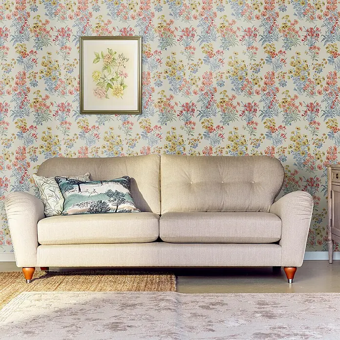 Laura Ashley Vliestapete Vliestapete Megan - Gelb, Floral - Helles beigefarbenes Stoffsofa mit Zierkissen in einem gemütlichen Raum mit Blumentapete.
