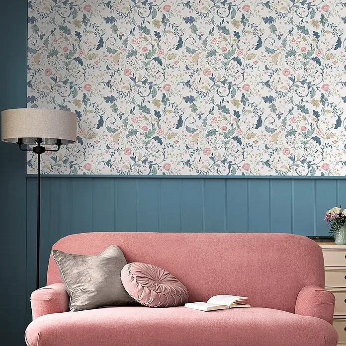 Laura Ashley Vliestapete Litton - Blau, Floral, 1.000 x 52 cm - Florale Tapete in Blau-, Grün- und Rosatönen auf weißem Hintergrund, schmückt eine Wohnzimmerwand über blauen Paneelen.