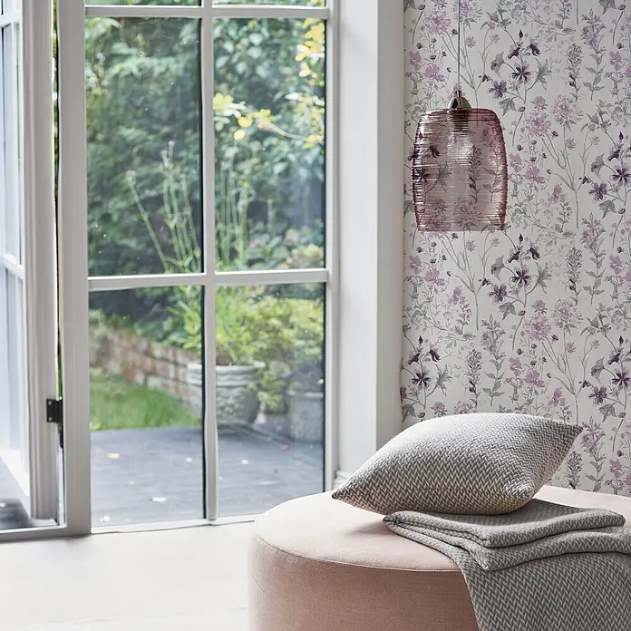 Laura Ashley Vliestapete Vliestapete Wilde Wiese - Rosa/Weiß, Floral - Ein rosafarbener Polsterhocker mit einem grauen Chevron-Kissen und passender gefalteter Decke.