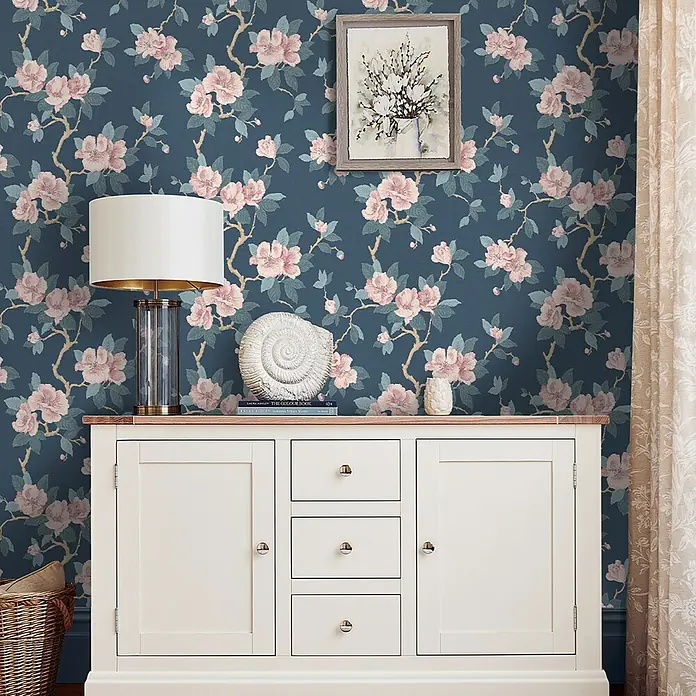 Laura Ashley Vliestapete orientalische Blüte - Blau, Floral, 1.000 x 52 cm - Dunkelblaue Blumentapete mit rosa Blüten und grünen Blättern, schmückt eine Wand über einem weißen Schrank.