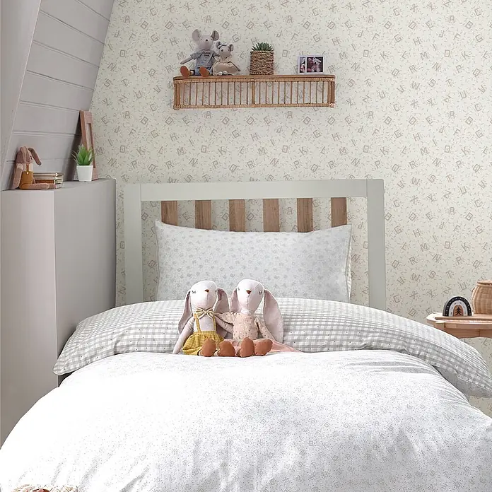 Laura Ashley Vliestapete Alphabet - Braun/Grau, Floral, 1.000 x 52 cm - Bettwäsche-Set mit Alphabet- und Laubmuster auf einem Bett im Kinderzimmer.
