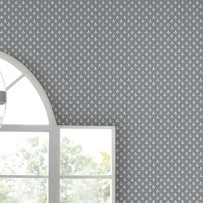 Laura Ashley Vliestapete Trefoil - Grau, Ornament, 1.000 x 52 cm - Graue Tapete mit kleinem weißen Blattmuster, an einer Wand neben einem Rundbogenfenster.