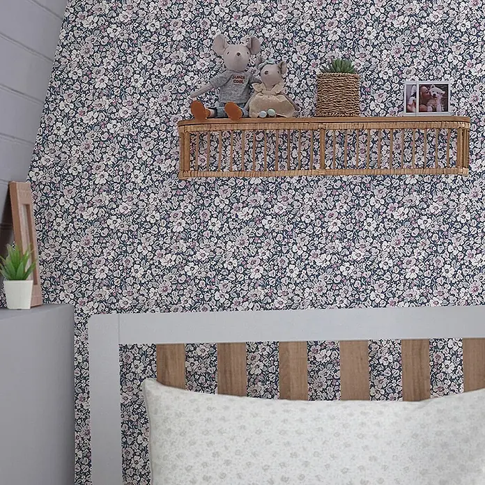 Laura Ashley Vliestapete Vliestapete Libby - Lila, Floral, 10 x 0,52 m - Florale Tapete mit kleinen weißen und lila Blüten auf dunkelblauem Grund, an einer Schlafzimmerwand über einem weißen Bett und einem Korbregal.