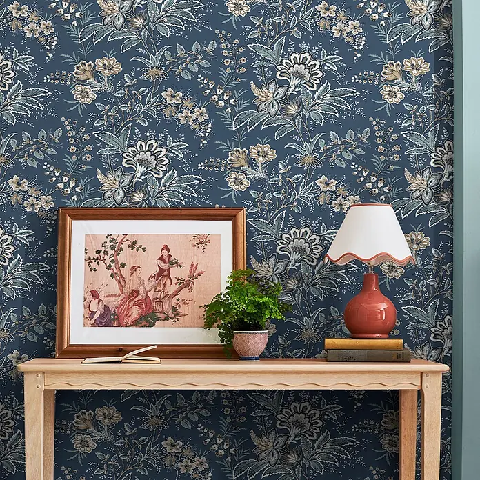Laura Ashley Vliestapete antikes Textil - Blau, Floral, 1.000 x 52 cm - Dunkelblaue Blumentapete als stilvolle Kulisse für einen Holzkonsolentisch mit Dekoration.