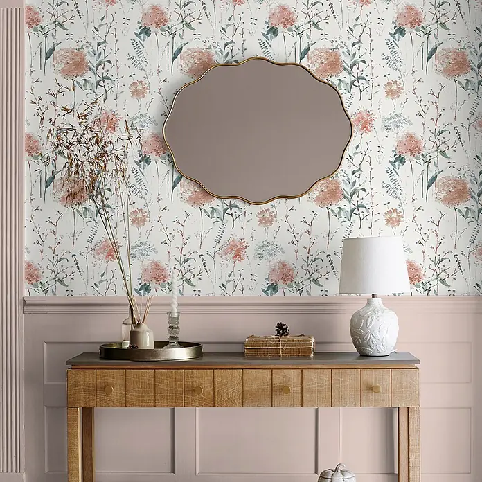 Laura Ashley Vliestapete Aquarell Blumen - Rosa, Floral, 1.000 x 52 cm - Hölzerner Konsolentisch mit geriffelten Schubladenfronten und dunkler Platte, in einem Raum mit Blumenmuster-Tapete und Spiegel darüber arrangiert.