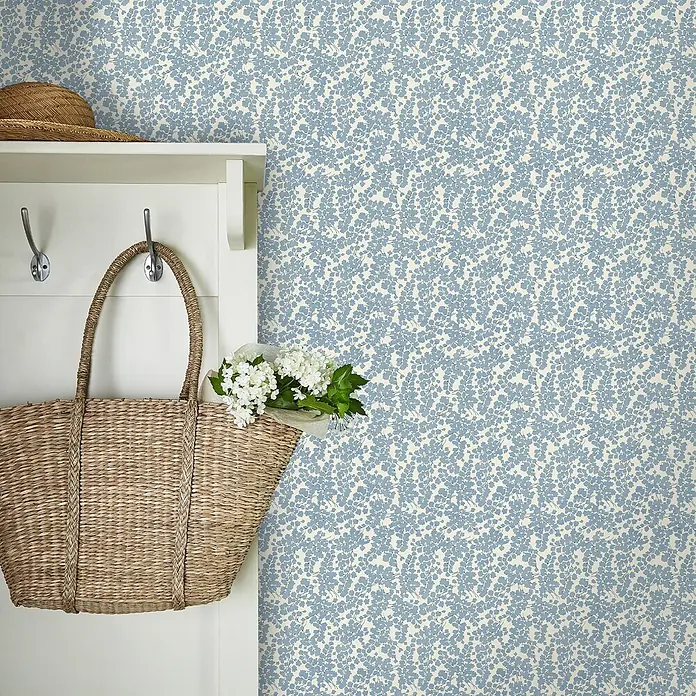 Laura Ashley Vliestapete Vliestapete Cariad - Blau, Floral, 10 x 0,52 m - Blau-weiß gemusterte Tapete mit kleinen botanischen Blattmotiven, an einer Wand in einer Wohnumgebung gezeigt.