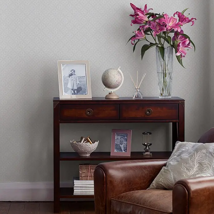 Laura Ashley Vliestapete Mr Jones - Weiß, Ornament, 1.000 x 52 cm - Helle, graue Tapete mit zartem geometrischem Muster an einer Wand, passend zu einer klassischen Konsole und einem Ledersessel.