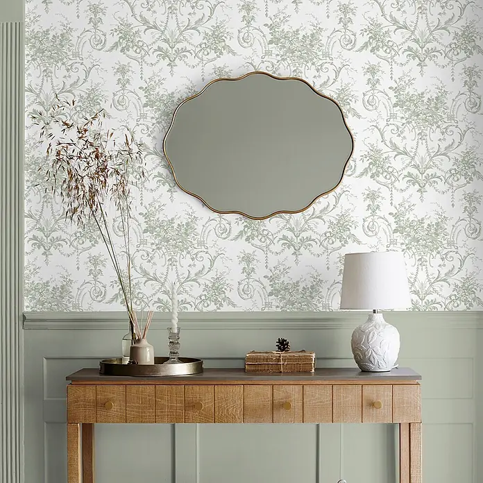 Laura Ashley Vliestapete Tuileries Französisch - Grün, Floral, 1.000 x 52 cm - Goldgerahmter Muschelspiegel hängt an gemusterter Tapete über einer Holzkonsole.