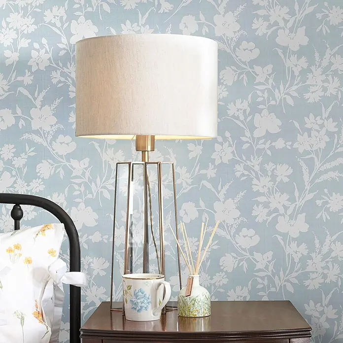 Laura Ashley Vliestapete Vliestapete Blumen Monoprint - Blau, Floral - Hellblaue Tapete mit weißem Blumenmuster hinter einer Nachttischlampe und einem Nachttisch.