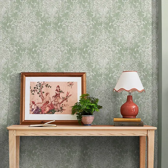 Laura Ashley Vliestapete ornamentales Motiv - Grün, Floral, 1.000 x 52 cm - Salbeigrüntapete mit einem verzierten, abgenutzten cremefarbenen Damastmuster, die eine Wand hinter einem Konsolentisch schmückt.